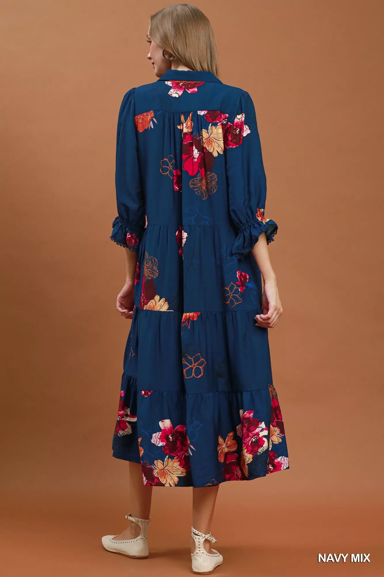 Woman wearing a navy dress with floral embroidery on a brown background