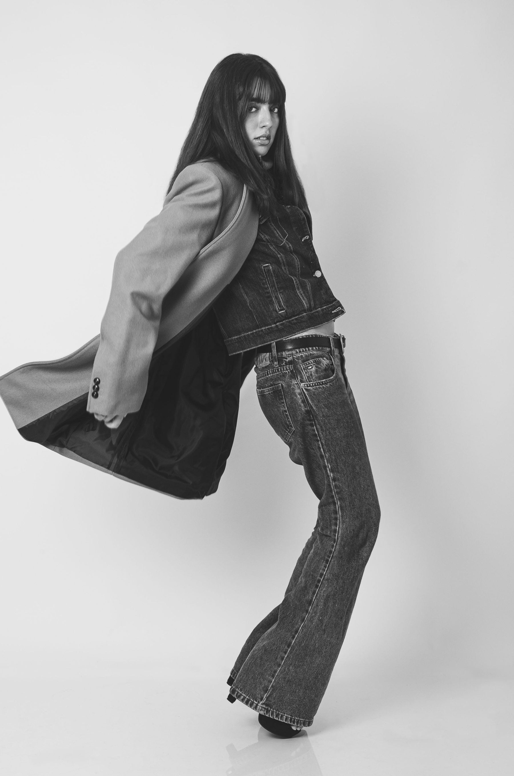 A model in a denim jacket, jeans and a tailored coat, mid-stride