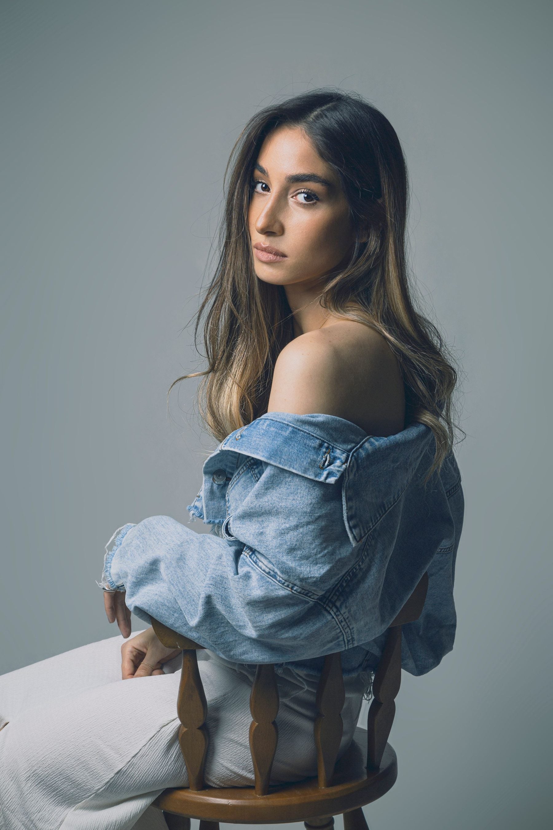 A model in a light wash denim jacket worn off the shoulder