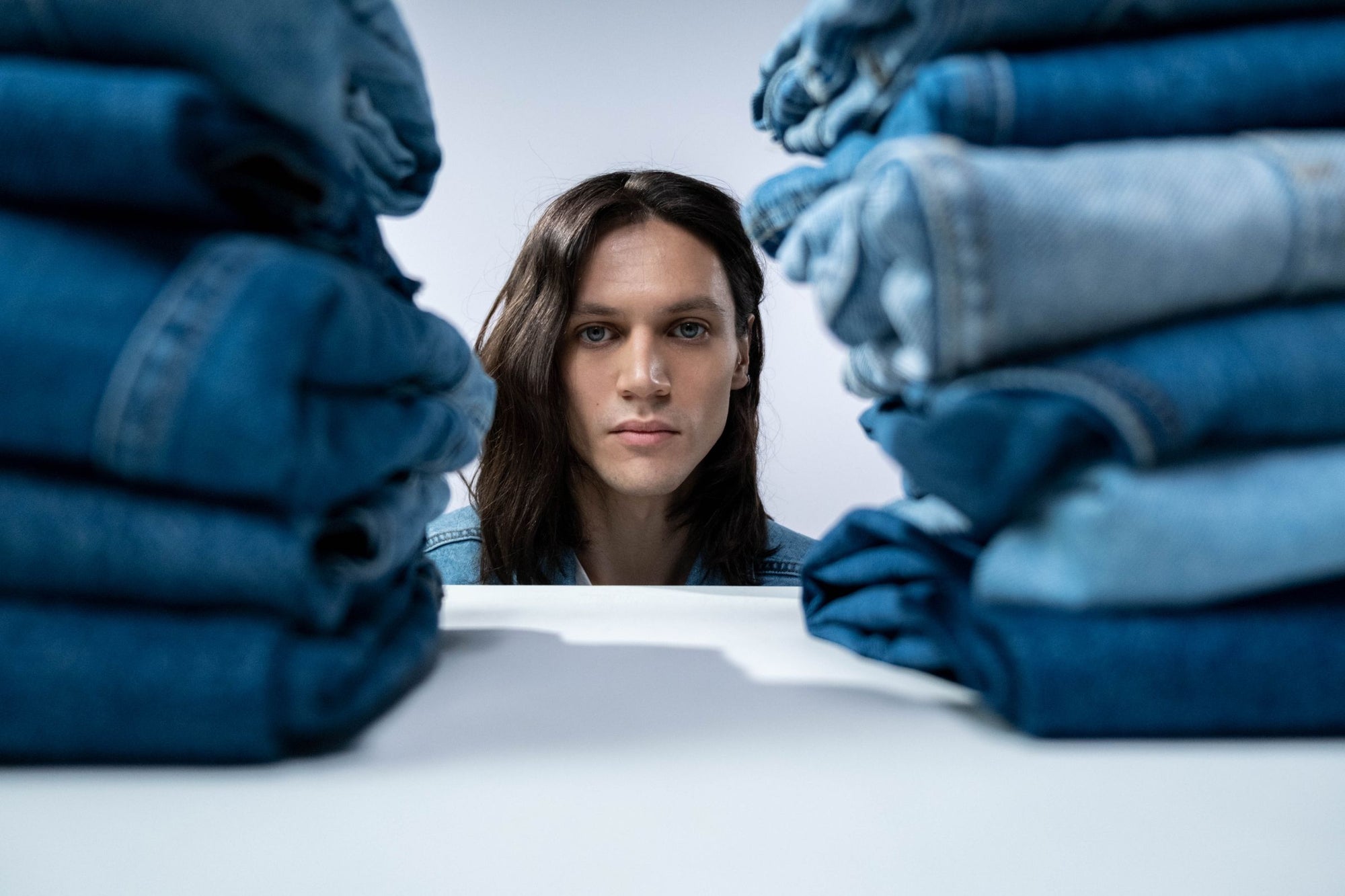 A model framed between stacks of folded denim